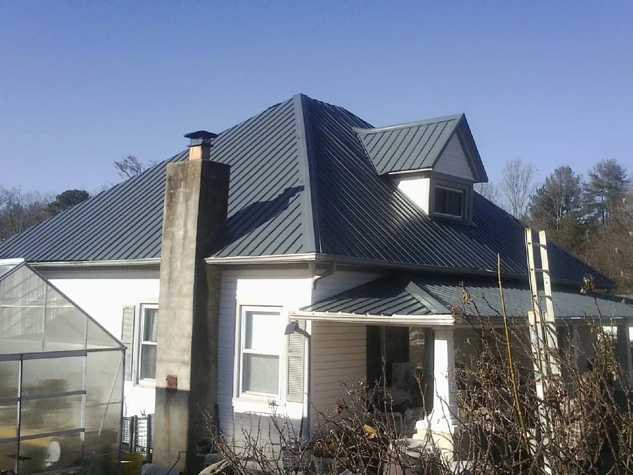 Dark blue standing seam metal roof on a white farmhouse with dormer — Slate & Tile Roof Repair by Roofing Brothers in Arkport