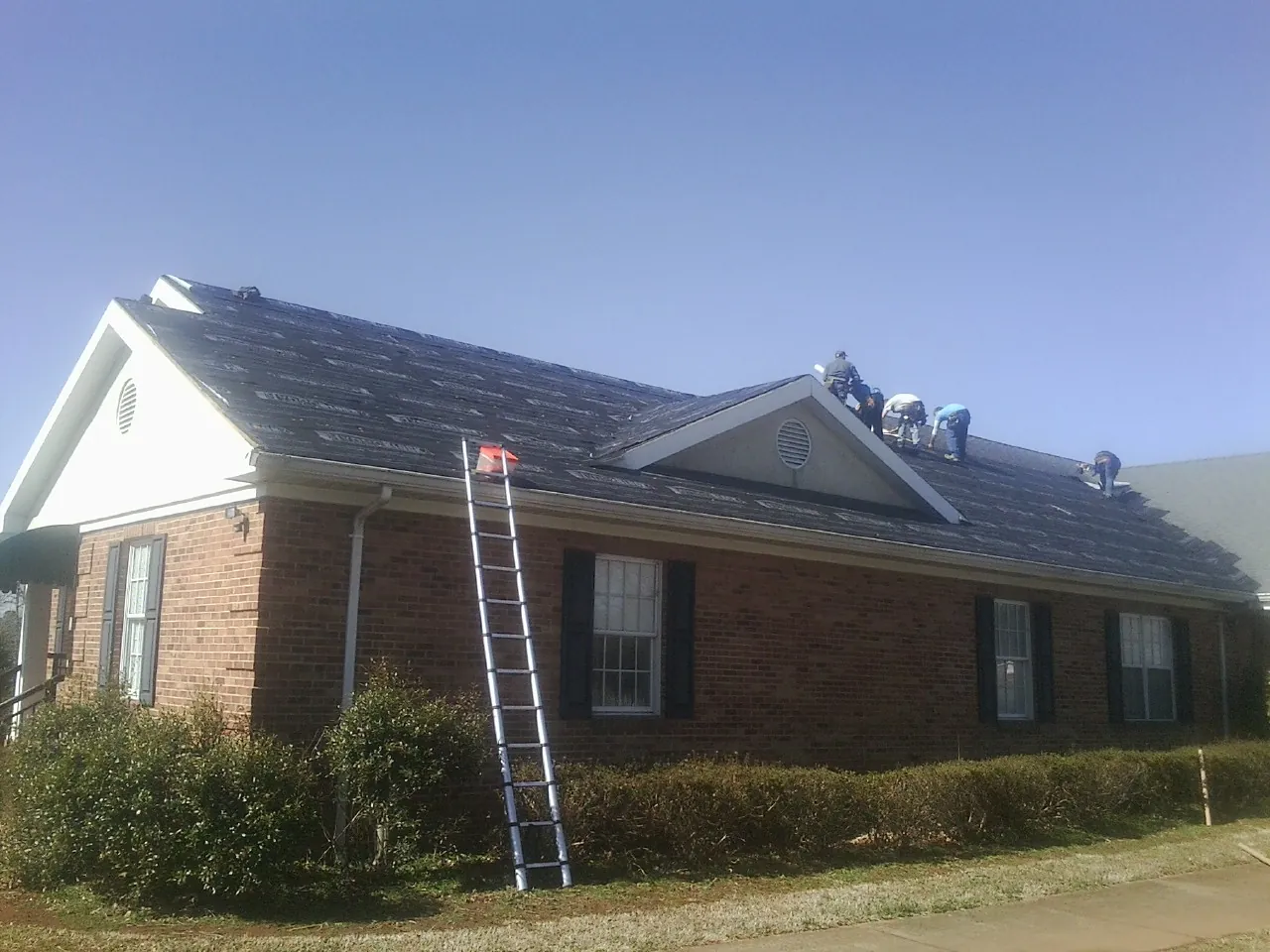 Crew tearing shingles off a brick ranch roof with a ladder set — Metal Roof Repair work by our crew in Arkport