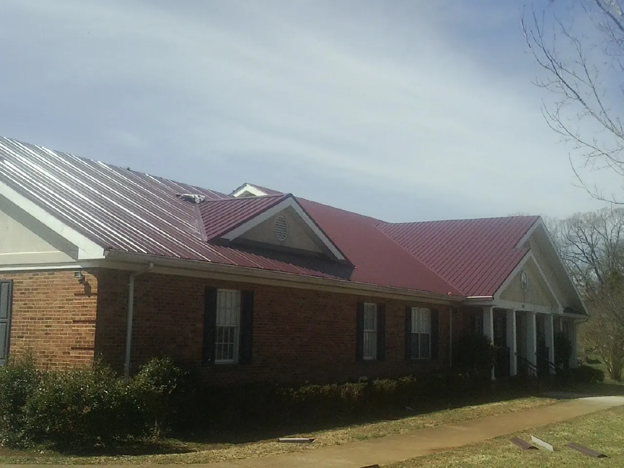 Red metal roof with gabled entries on a long brick building, from a Hail Damage Roof Repair job in Arkport