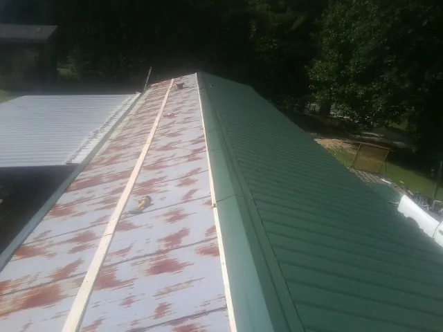Old rusted panels beside newly installed green metal roofing — Wind Damage Roof Repair by Roofing Brothers in Arkport