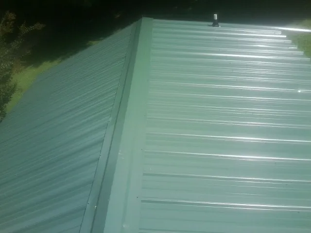New green metal panels meeting at the ridge of a roof — Flat Roof Repair work by our crew in Arkport