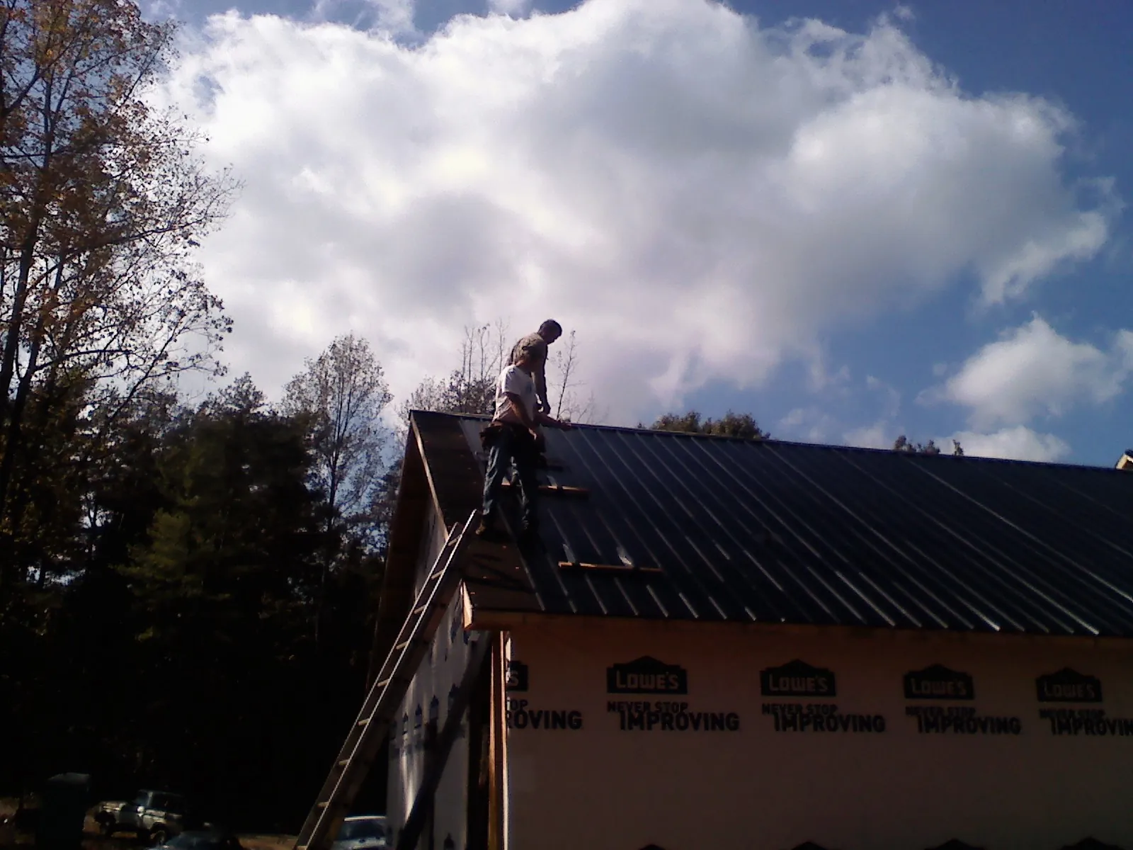 Roofer fastening dark metal panels high against a cloudy sky, from a Roof Inspection job in Arkport